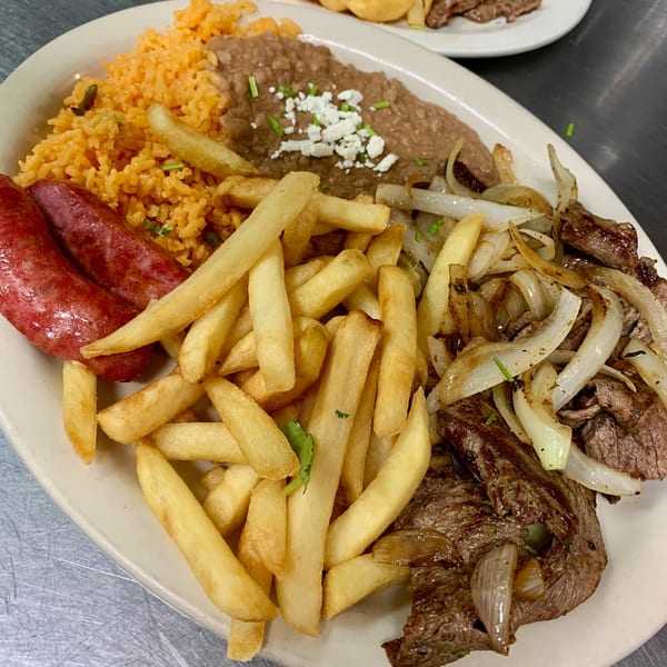 La Tiendita's Mexican dish with steak, onions, fries, sausages, rice, and refried beans.