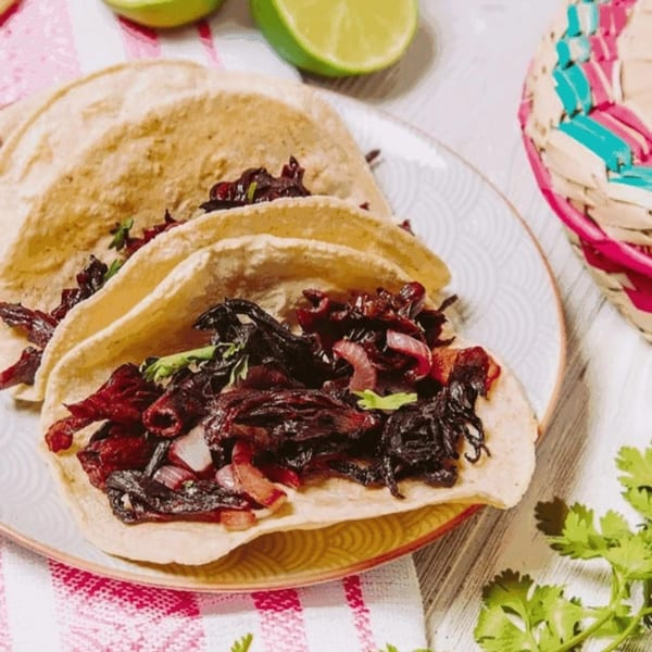 Three La Tiendita Mexican Restaurant tacos with dark red filling, red onions, and cilantro.