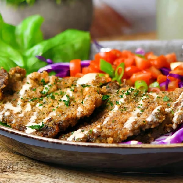 Crispy breaded meat drizzled with white sauce, garnished with parsley, served with diced tomatoes and red cabbage.