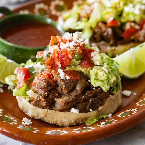 Two La Tiendita sopes with meat, lettuce, guacamole, pico de gallo, and cheese, with a side of salsa.