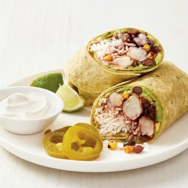 Two shrimp burritos, cut in half, with sour cream, lime wedges, and pickled jalapeños on a white plate.