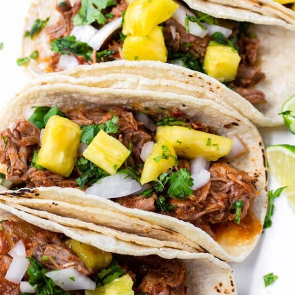Three La Tiendita Mexican Restaurant tacos filled with meat, pineapple, onions, and cilantro.