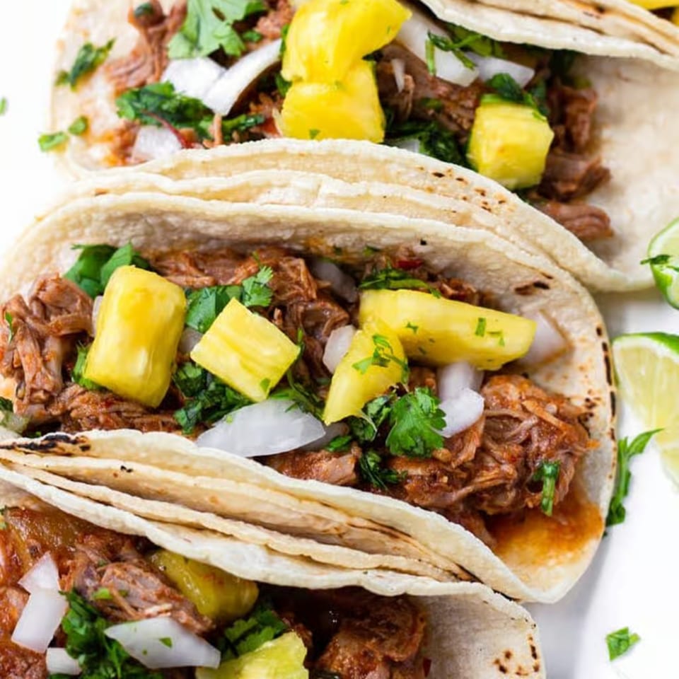 Three La Tiendita Mexican Restaurant tacos filled with meat, pineapple, onions, and cilantro.