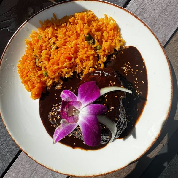 La Tiendita's chicken mole with orange rice, sesame seeds, onion, and a purple orchid garnish.