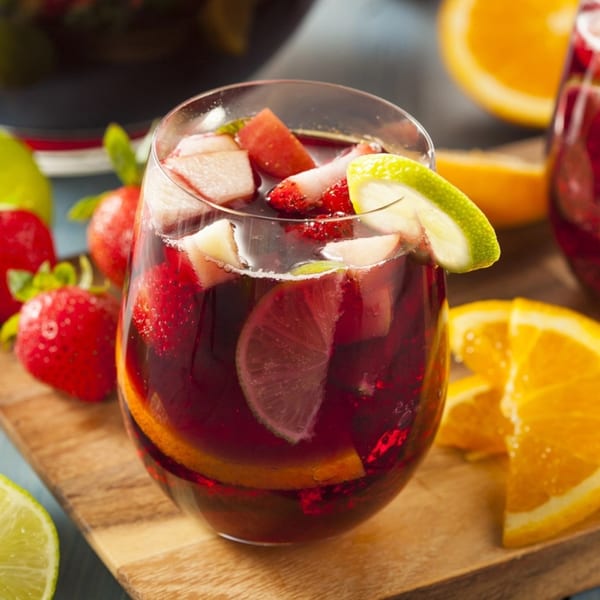 A glass of La Tiendita's red sangria with fruit slices and strawberries on a wooden board.